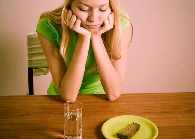 Девушка сидит перед стаканом воды и хлебом
